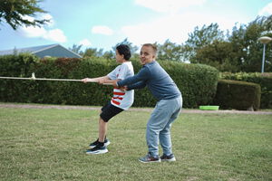 Zwei Jungen spielen gemeinsam im Freien und halten lachend ein Seil - ein Moment von Bewegung, Freude und gemeinschaftlicher Teilhabe auf einer gruenen Wiese.