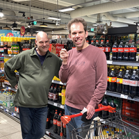 "Thilo steht mit einer anderen Person im REWE vor dem Getränkeregal."