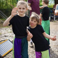 "Ava und ein anderes Kind in Zirkusoutfit winken in die Kamera"