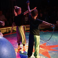 "Ava steht auf der Zirkusbühne neben einer anderen Person, welche ein Seil in der Hand hat."