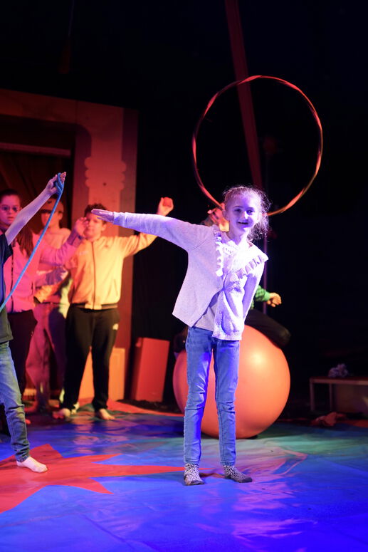 "Ava auf der Zirkusbühne mit einem Arm zur Seite gestreckt"