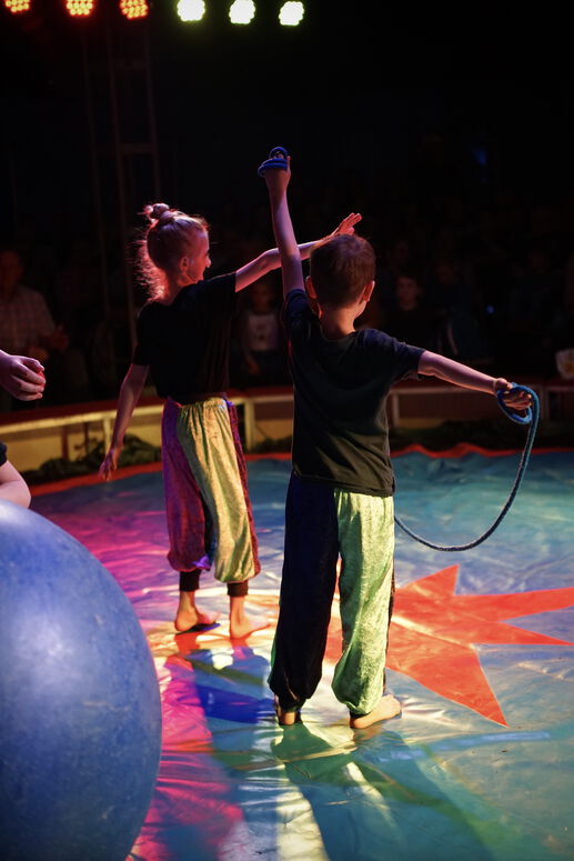 "Ava steht auf der Zirkusbühne neben einer anderen Person, welche ein Seil in der Hand hat."